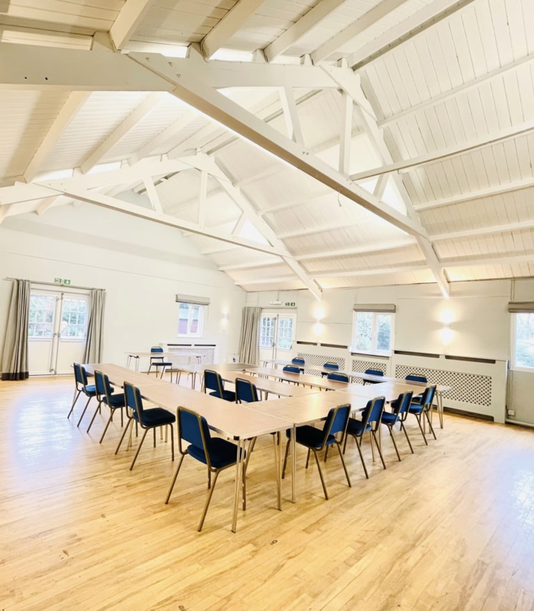 A vaulted meeting room with exposed white roof beams, set out with tables and chairs
