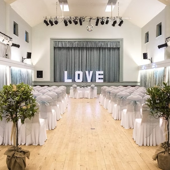 The main hall dressed for a wedding, with white chair covers and light-up LOVE letters on stage