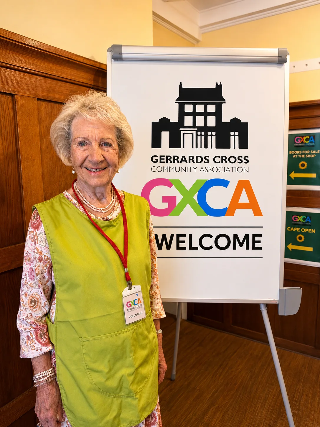A GXCA volunteer welcoming visitors beside a GXCA welcome sign