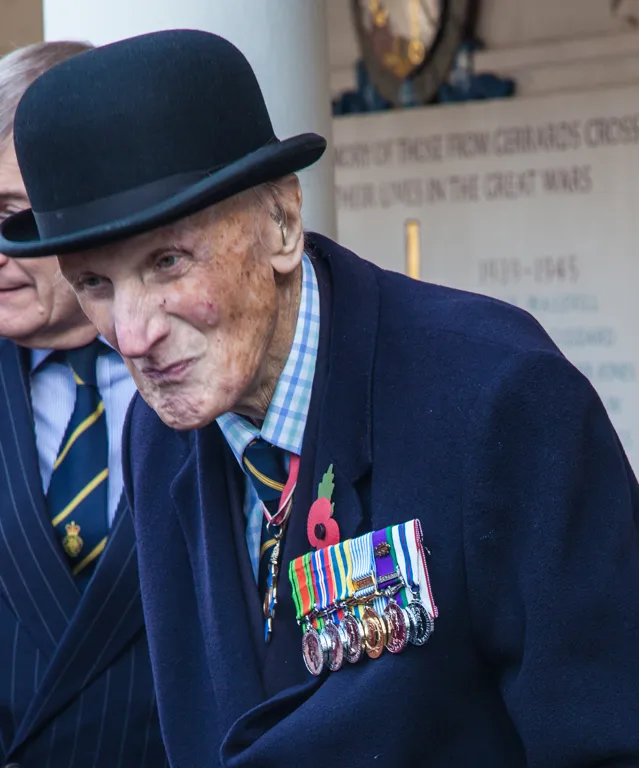 An elderly veteran in a bowler hat and medals in front of the Roll of Honour