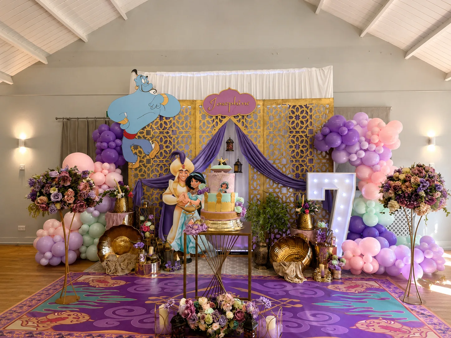 A genie-themed birthday backdrop with a balloon arch and a light-up number 7