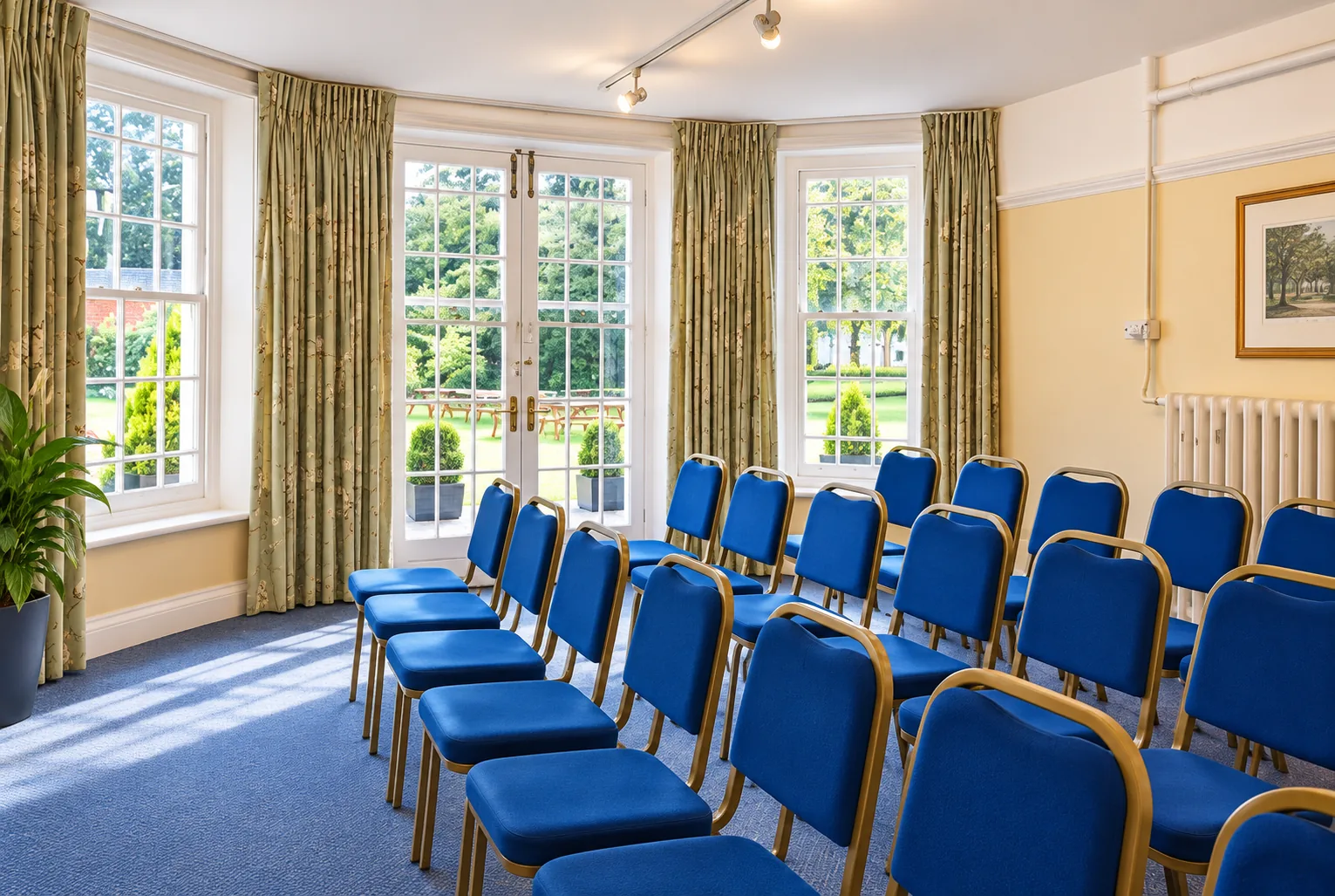 Room 6 set out with rows of blue chairs beside tall windows onto the garden
