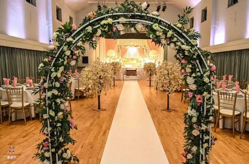 A floral arch over a white aisle leading to a decorated stage in GXCA’s hall