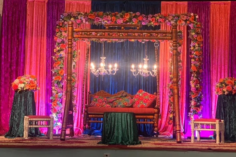 An ornate carved wooden swing stage framed with flowers and pink drapes for a mehndi