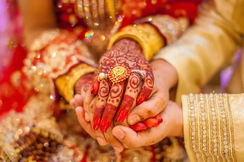 Close-up of a bride’s henna-decorated hands and gold jewellery, held by the groom