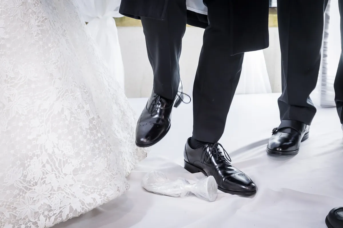 A Jewish groom’s foot breaking the glass beside the bride’s gown during the ceremony