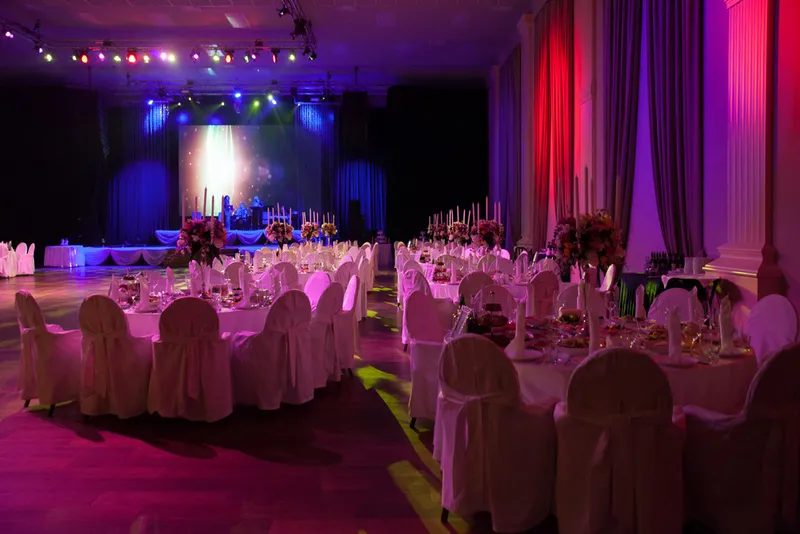 GXCA’s Colston Hall dressed for an evening reception with white linen tables, chair covers and coloured uplighting