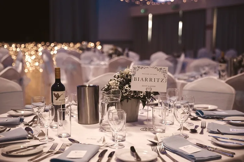 A wedding table at GXCA set with blue linens, a floral centrepiece and a printed table name