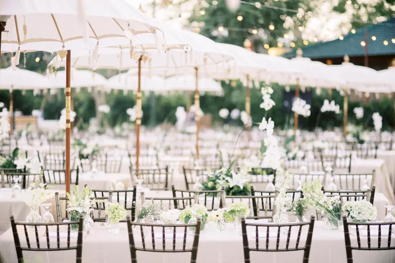 Long tables laid under white parasols with fairy lights for an outdoor wedding dinner